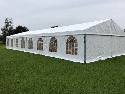 Un grand chapiteau blanc installé sur une pelouse verte. Le chapiteau est de grande taille et semble prêt pour un événement en plein air. Il y a des fenêtres en forme d'arcs sur le côté, laissant entrer la lumière naturelle.